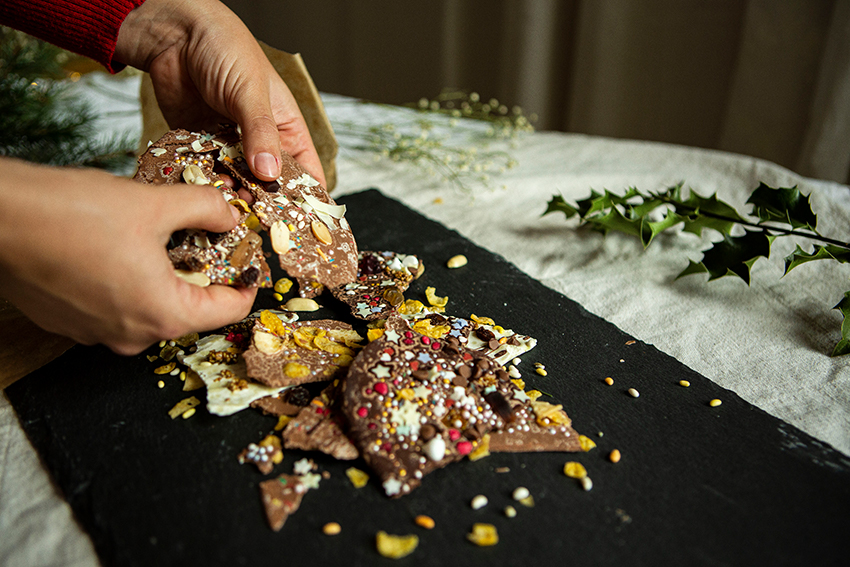De versierde chocolade wordt door twee handen op een plaat gebroken.