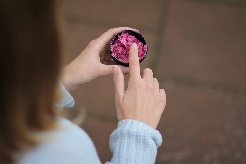  Een vinger haalt een kleine hoeveelheid blush uit een potje.