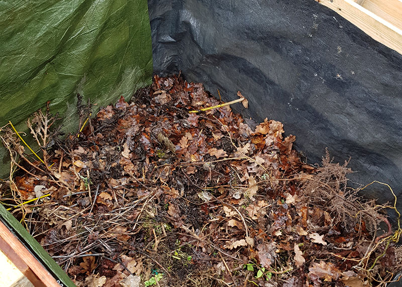 Das Hochbeet ist bis zur Hälfte gefüllt, man sieht die Gartenabfall-Schicht aus Laub und Geäst.