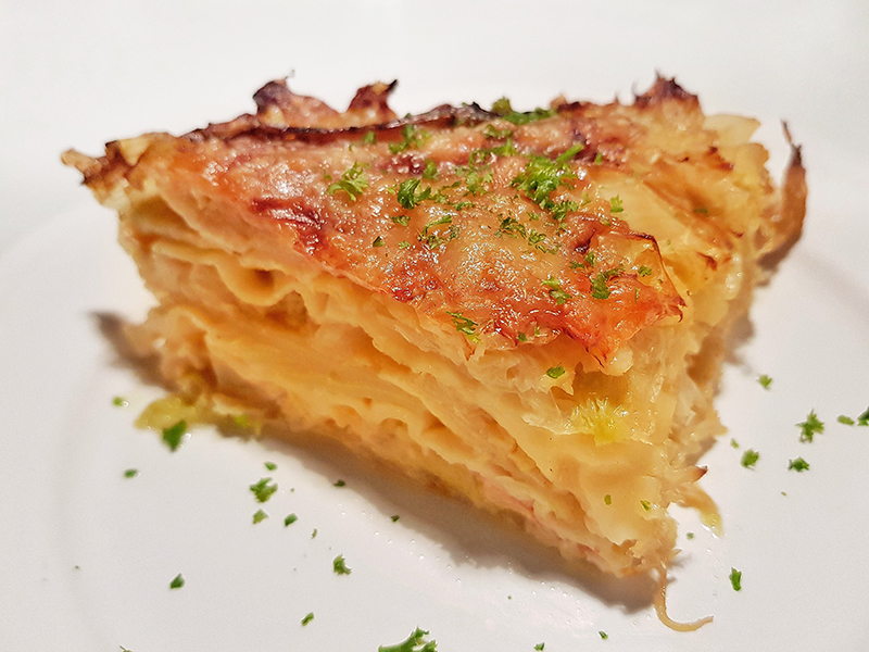 Goldgelb leuchtet das Stück Wirsinglasagne, das mit ein paar grünen Kräutern bestreut ist.