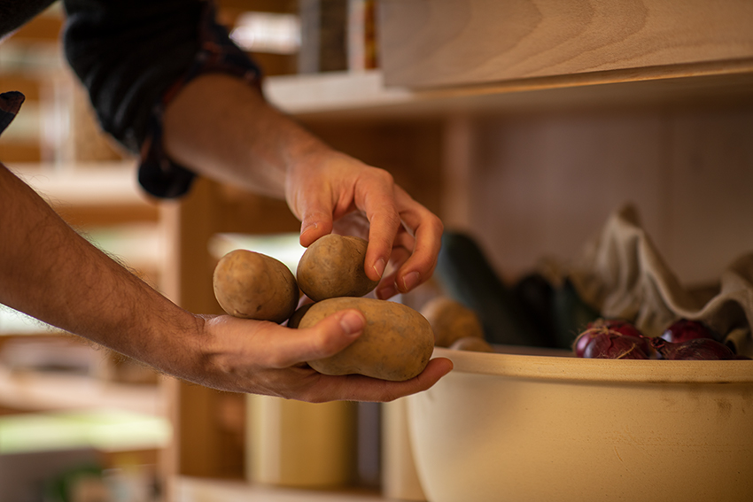 Drie opgeslagen aardappelen worden uit een afgedekte pot gehaald.