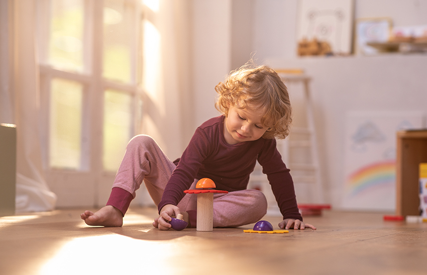 Ein Kind sitzt auf dem Boden und spielt mit buntem Holzspielzeug.