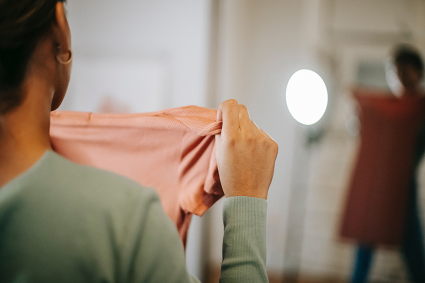 Frau steht vor dem Spiegel und hält sich ein Kleid vor den Körper.