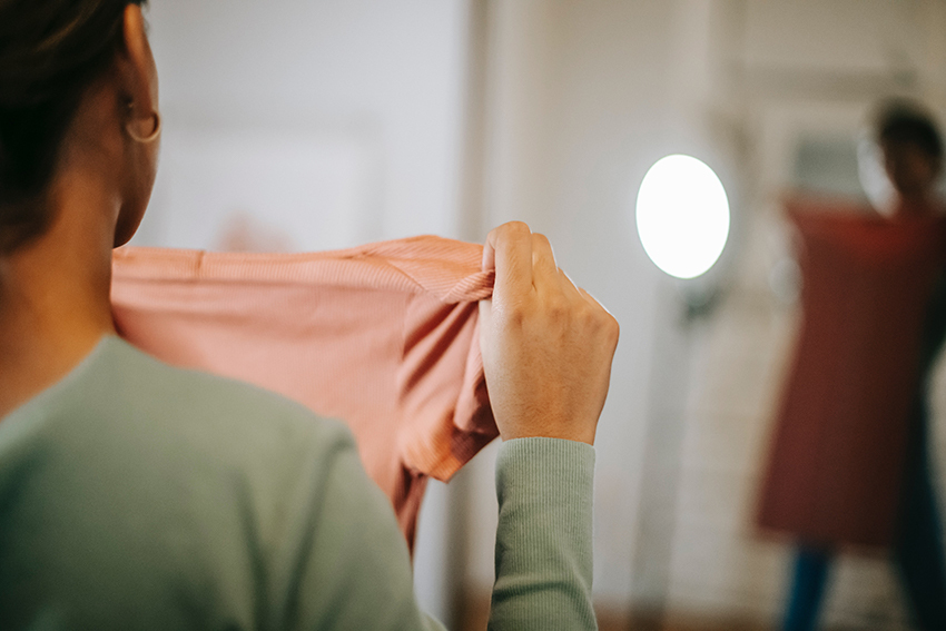 Vrouw staat voor de spiegel en houdt zich een jurk voor.