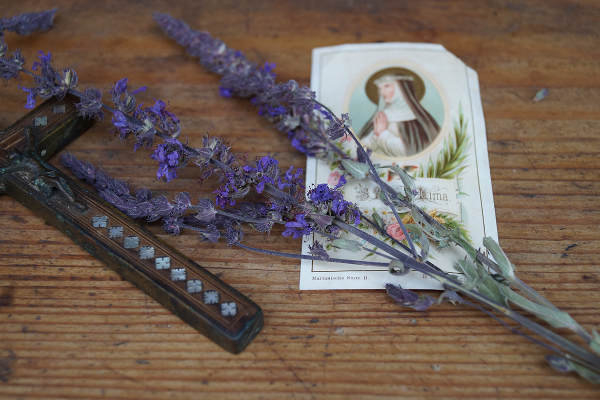 Ein Blutweiderich liegt neben einer Marienkarte und einem Kreuz.