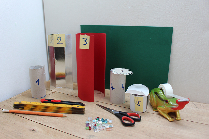De materialen voor de DIY caleidoscoop liggen op de grond en zijn genummerd.