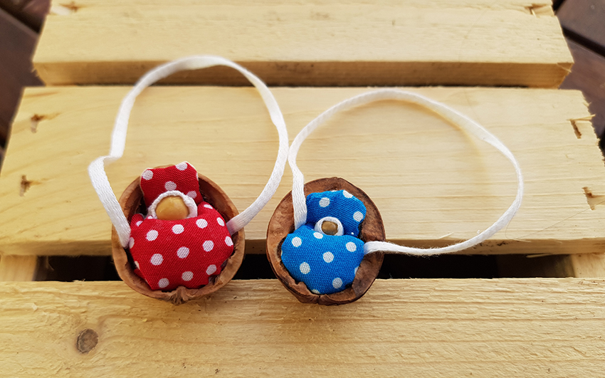 Ein rotes und ein blaues Deckchen in den zwei Nussschalen. der Aufhänger ist ein weißes Stoffband.