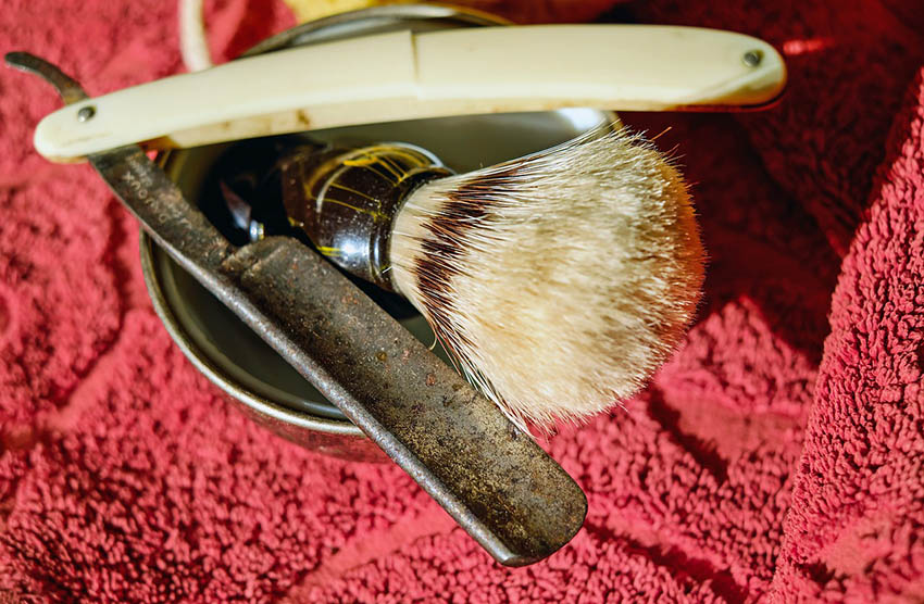 Close-up van een open scheermes met scheerkwast op rode handdoek