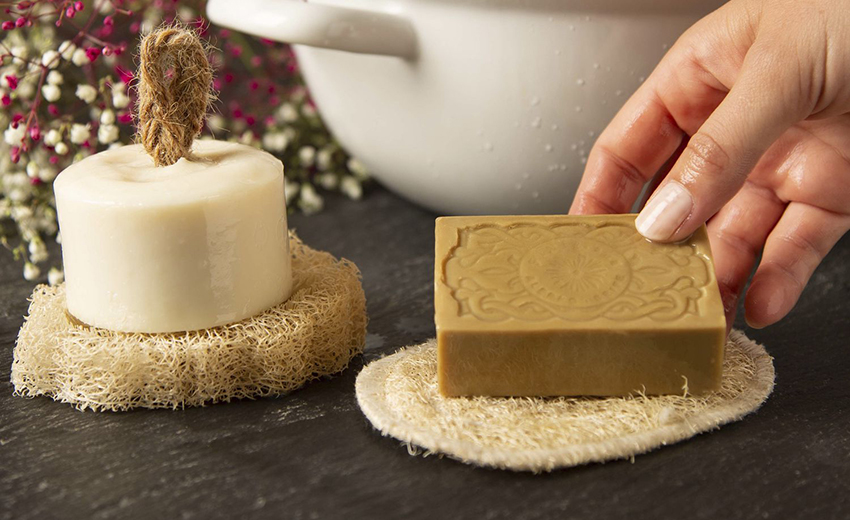 Een hand legt een stuk zeep op een luffa zeepkussen