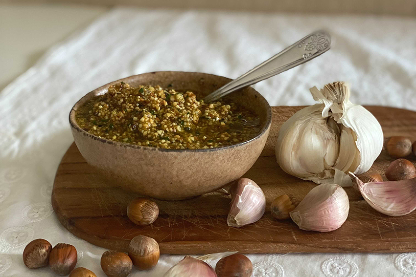 Een kom zelfgemaakte hazelnootpesto staat klaar, hazelnoten en knoflook liggen ernaast.
