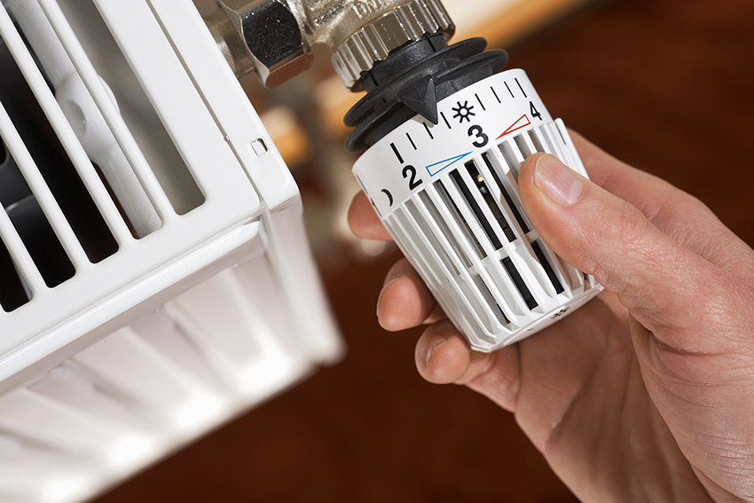Eén hand draait aan de thermostaat van de radiator.