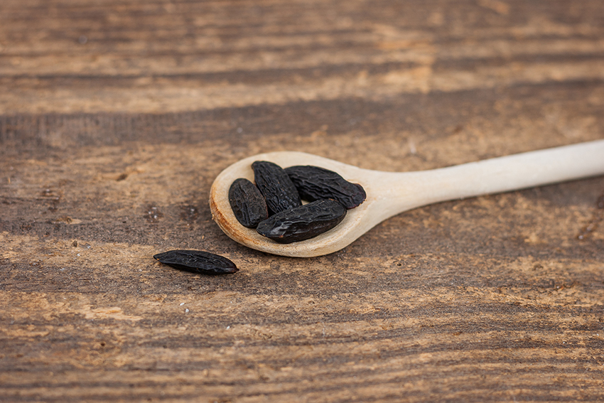 Die länglichen fast schwarzen Bohnen liegen auf einem Holzlöffel.