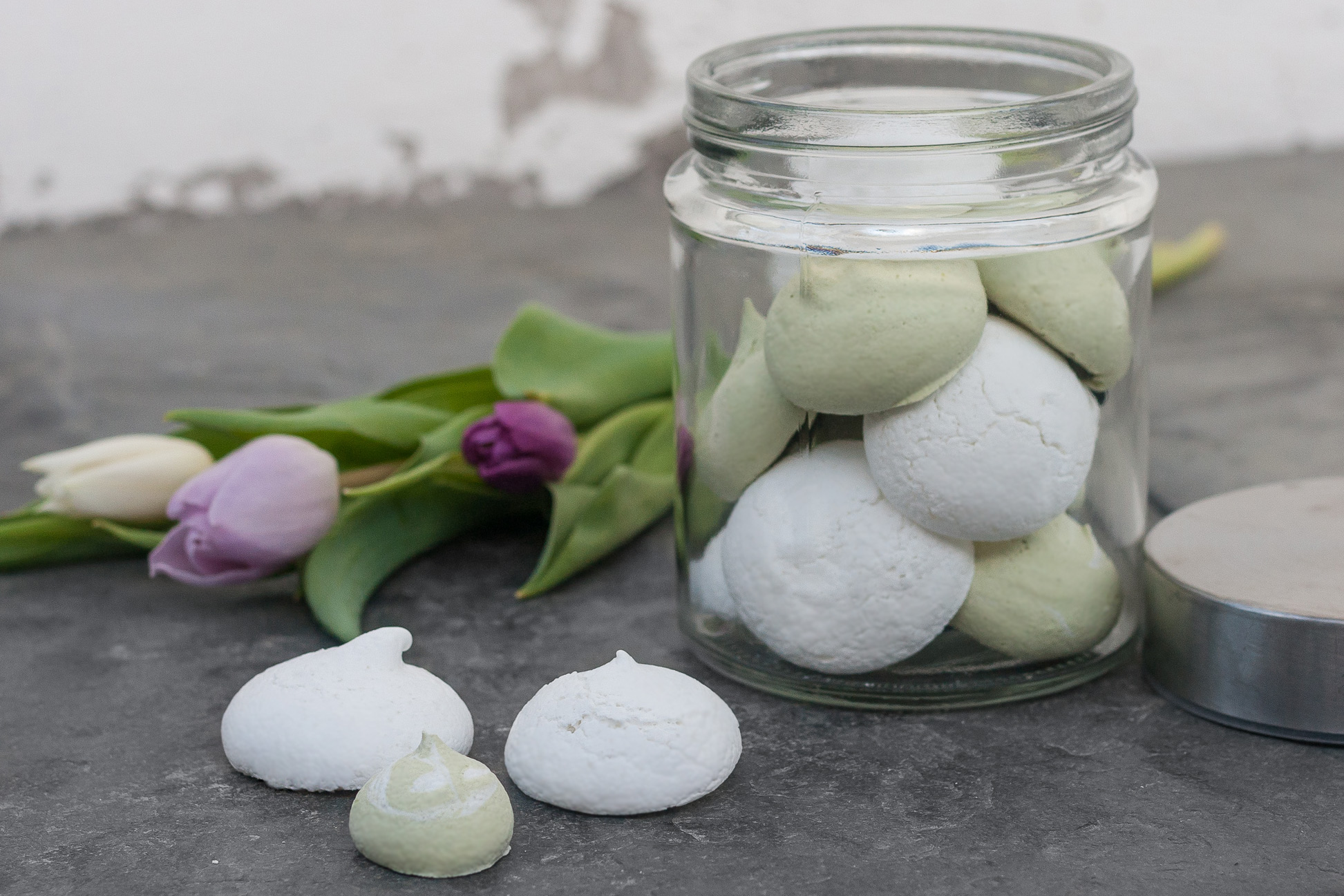 Weißes und grünes Baiser in einem Glas und davor, mit Tulpen im Hintergrund