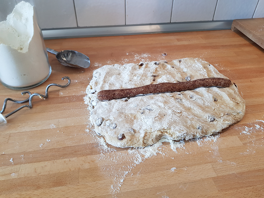Das Dattelmarzipan wird als lange Stange auf den veganen Quarkstollen gelegt.