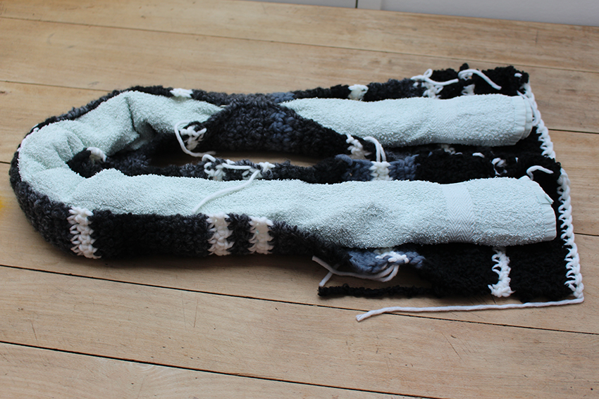 De gehaakte tochtrol ligt open op tafel en wordt opgevuld met een opgerolde handdoek.