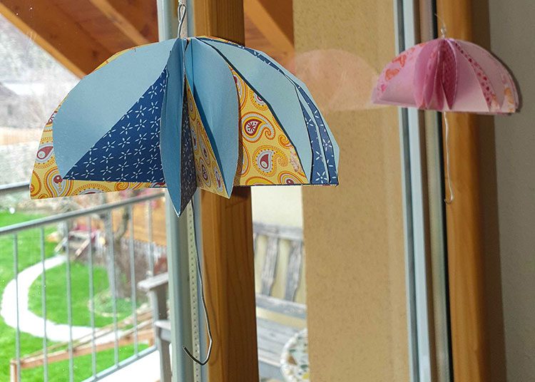 Zwei Regenschirme aus Papier hängen vor dem Fenster.