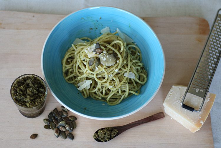 Das Kürbiskern-Pesto ist unter eine Portion Nudeln auf einem blauen Teller gemischt. 