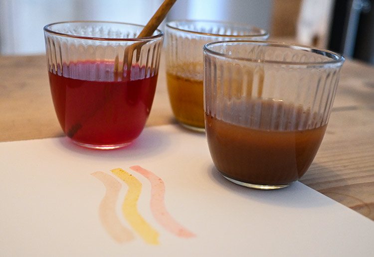 Auf einem Blatt wurde mit Naturfarben gemalt, die Farben stehen in Gläsern daneben.