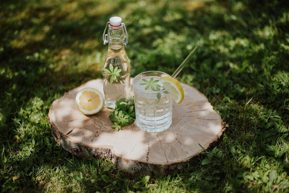 Ein Glas und eine Flasche mit selbst gemachtem Waldmeister-Sirup stehen auf einer Wiese.